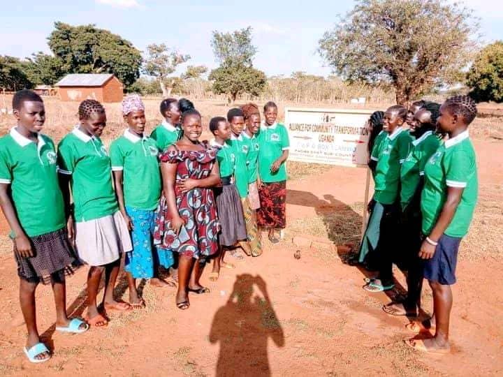 ACT Uganda staff and volunteers in green branded t-shirts standing beside the organization's signpost