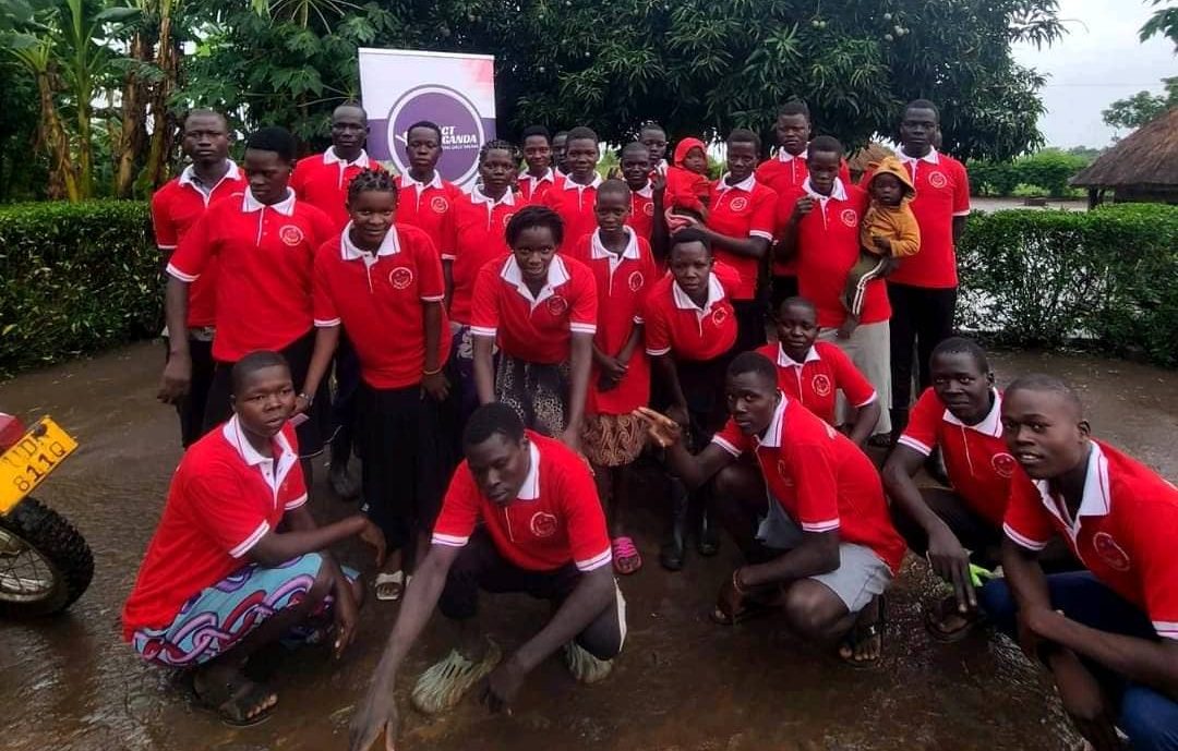 A group of ACT Uganda youth volunteers in red branded polo shirts posing together outdoors