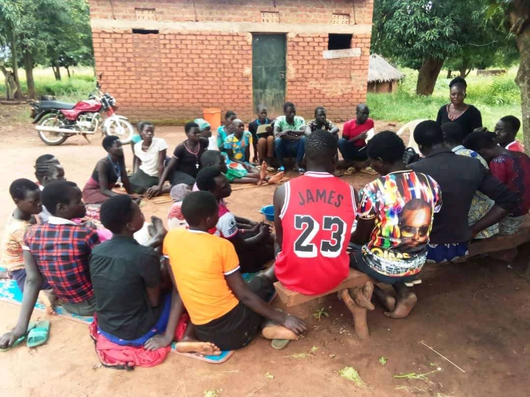 Community members sitting in a circle outdoors during an ACT Uganda community dialogue session in Padibe East Sub-county