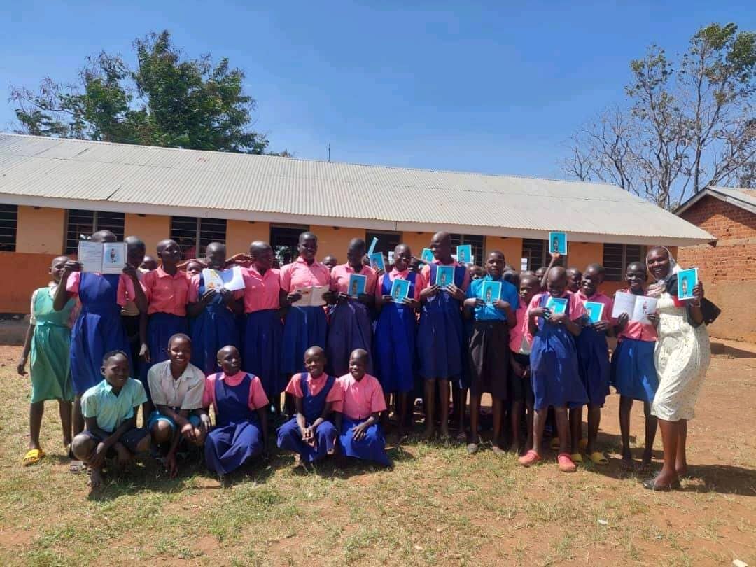 A large group of schoolgirls and boys holding copies of the ACT Uganda SRHR handbook outside their school
