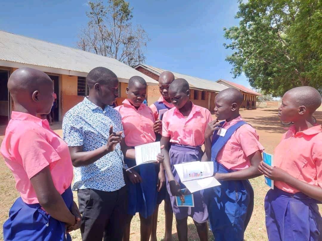 An ACT Uganda mentor speaking with a group of schoolgirls in pink uniforms during a mentorship session in Padibe East Sub-county